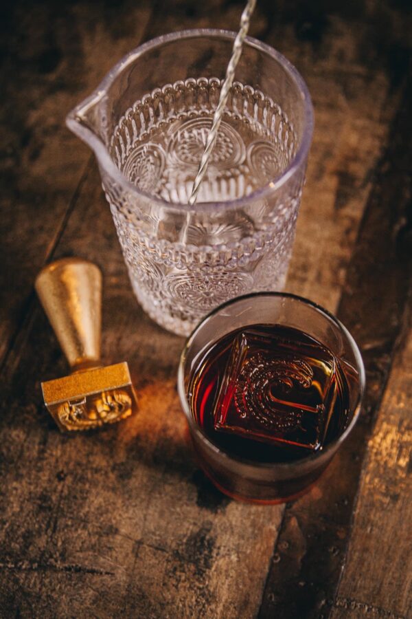 cocktail glass with whiskey and j ice cube stamp